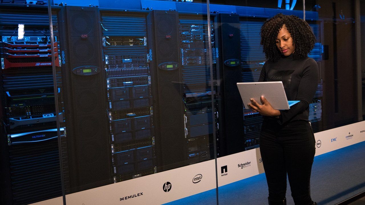 woman-standing-while-carrying-laptop-1181354-1 cybersecurity expert on a laptop ion front of servers