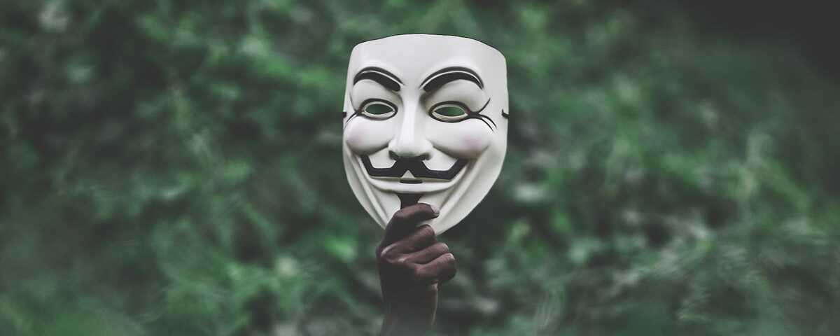 A hand holding up the recognizable anonymous mask.