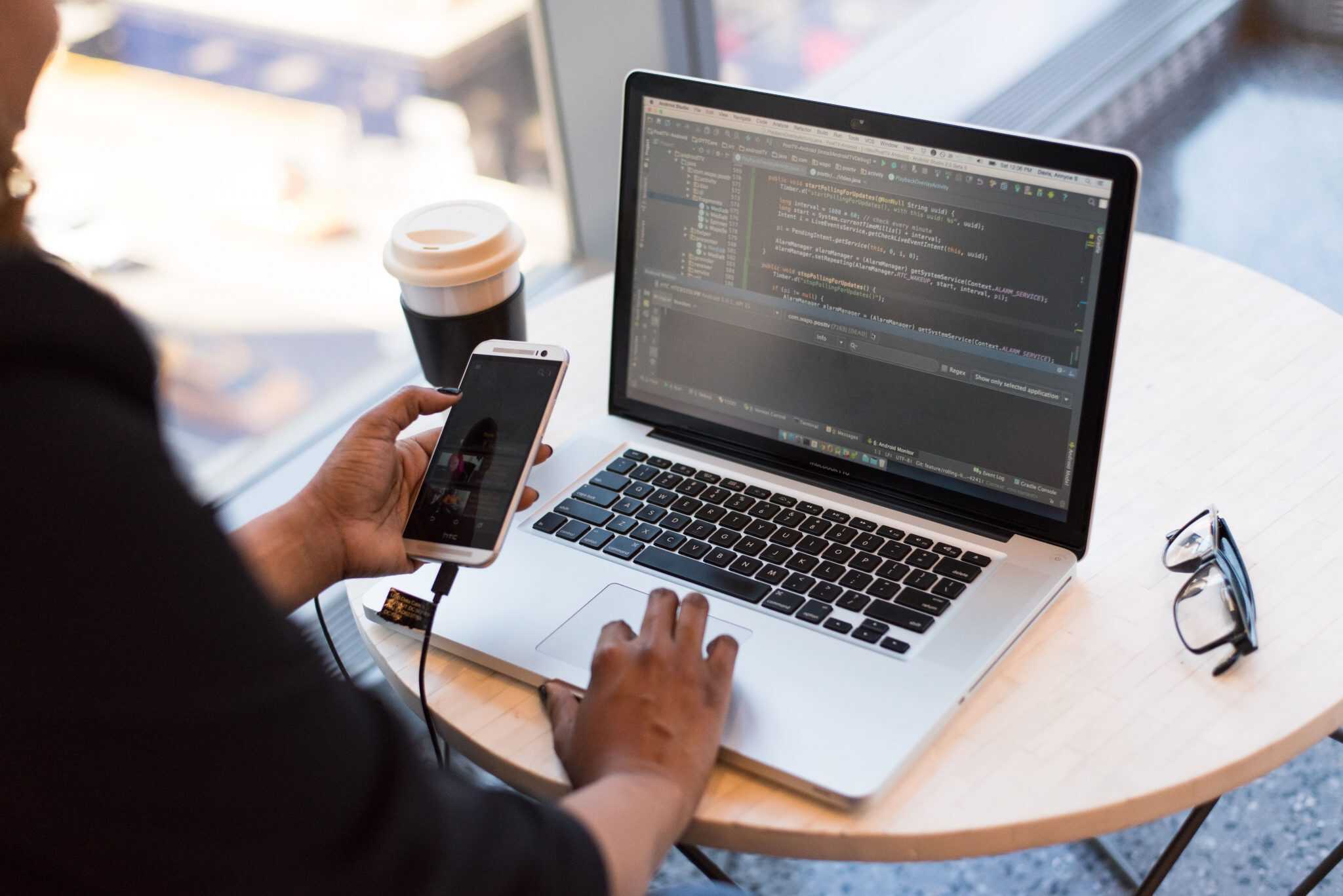 A person in a coffee shop. They are using their phone and laptop