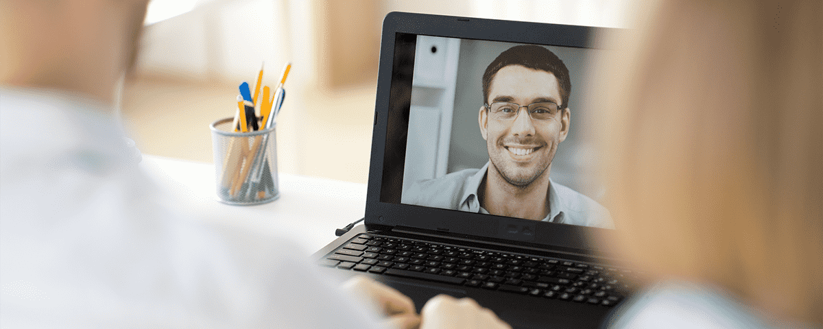 3 people having a video conference together. Two in the same room, the other on a laptop screen.